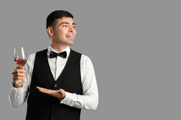 Young sommelier with glass of wine on grey background