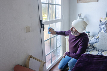 Mature man wiping condensation off bedroom window with a cloth. Problems with humidity, mould,...