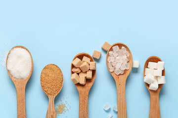Spoons with different types of sugar on blue background