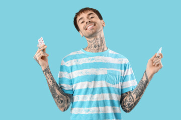 Allergic young man with nasal drops and pills on blue background