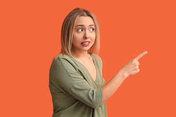 Young woman feeling shame while pointing at something on orange background