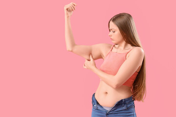 Young woman with chubby arms on pink background. Weight gain concept