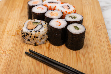 Wooden board with a variety of sushi rolls on it. The sushi rolls are of different colors and sizes, and there are chopsticks next to them. Concept of variety and abundance
