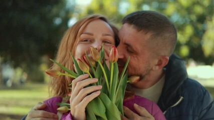 Romantic couple enjoying time together in park, holding tulips and expressing affection.International women's day