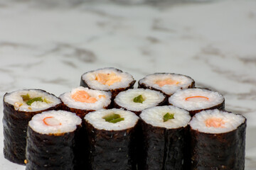 Row of sushi rolls with different fillings, including shrimp, avocado, and cucumber. The rolls are arranged in a neat row on a white countertop