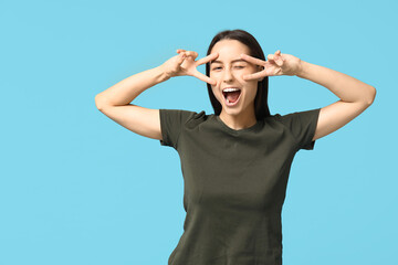 Beautiful young woman showing victory gesture on blue background