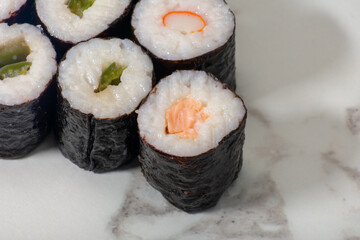Row of sushi rolls with different fillings, including shrimp, avocado, and cucumber. The rolls are arranged in a neat row on a white countertop
