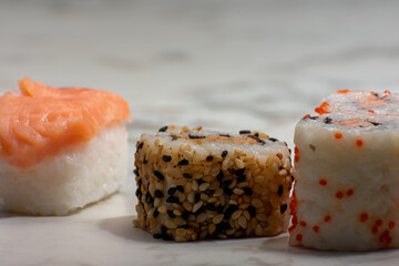 Sushi rolls rest on a white surface, featuring a variety of toppings including salmon, sesame seeds, and vibrant orange fish roe, creating a colorful and appetizing display.