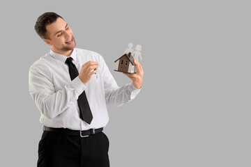 Male realtor with keys and house model on light background