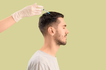 Fototapeta premium Young man receiving injection for hair growth on green background, closeup