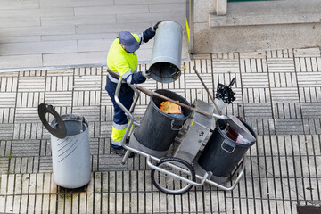 Cleaning worker emptying the trash into his cleaning cart on a city sidewalk