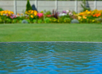 niebo odbite w szklanym blacie stołu na tle ogrodu z  trawnikiem i kwiatami, sky reflected in the glass table against the background of garden with flowers, blue sky reflected in glass table, iluzja 