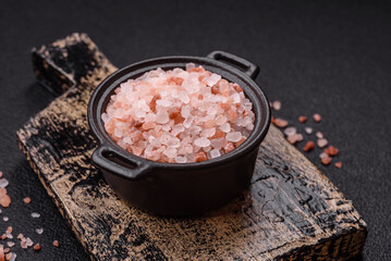 Pink himalayan salt in a black bowl on a dark concrete background