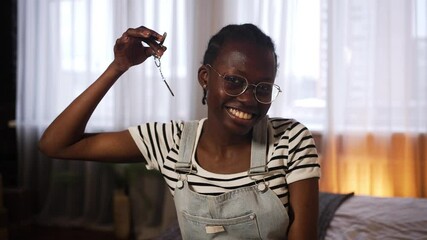 Young african american woman holding house keys with keychain, beaming with pride in newly purchased home, symbolizing personal achievement and independence - Powered by Adobe