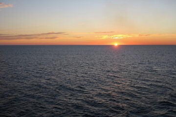 Obraz premium Die Sonne geht unter über dem Skagerrak an einem schönen Sommertag. Die Wellen sind dunkel, und die teils untergegangene Sonne taucht den Himmel in orangefarbenes Licht. Gesehen von einer Fähre.