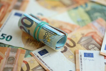 Roll of twenty euro currency bills lies on big amount of hundred and fifty euro banknotes