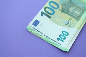 Big amount of one hundred euro money bills on lilac background