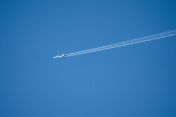 twin engined jet liner aircraft in deep blue sky, contrails vapour trails