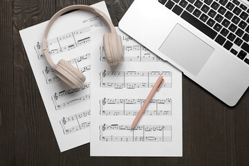 Music sheets with laptop and headphones on wooden background