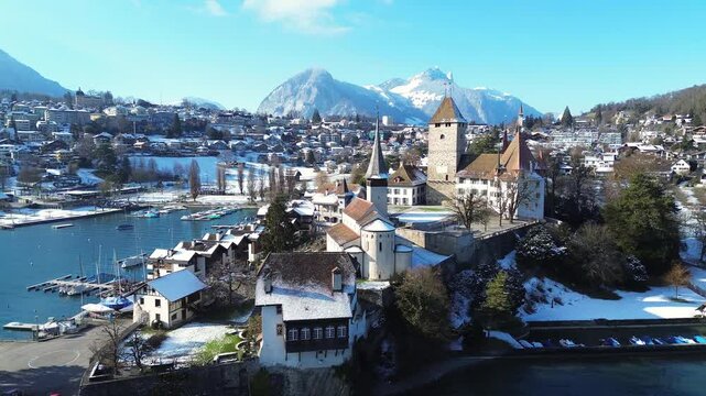 Spiez Castle during a snowy winter, surrounded by the Lake Thun, buildings, and the Swiss Alps