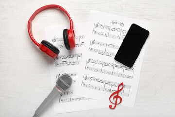 Modern mobile phone, music sheets, headphones and microphone on white wooden background
