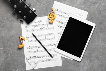 Composition with music sheets, guitar, modern tablet computer and earphones on grunge background