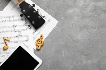 Composition with music sheets, modern tablet computer, earphones and guitar on grunge background