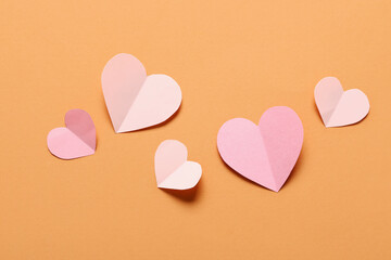 Composition with pink paper hearts on orange background. Valentine's Day celebration