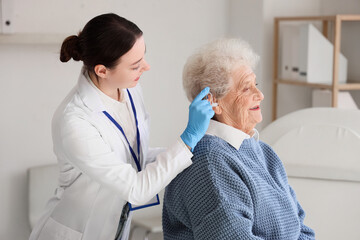 Obraz premium Female doctor putting hearing aid in senior woman's ear at hospital