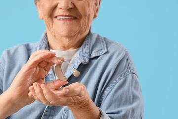 Fototapeta premium Senior woman with hearing aid on blue background, closeup