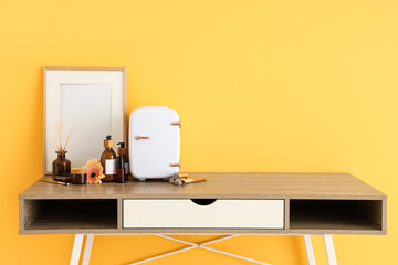 Table with small cosmetic refrigerator, frame and flower against yellow background. Closeup