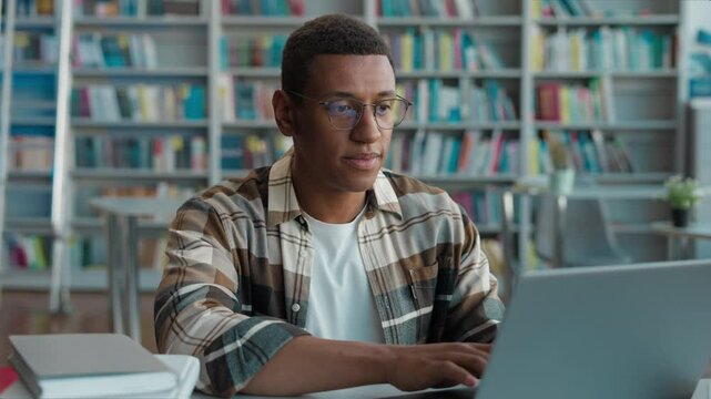 African American man guy male typing browsing laptop online computer high school library university student studying learning e-learning looking at camera smiling internet networking texting college