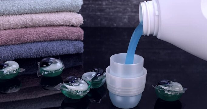 Liquid detergent flowing from the bottle into the container in front of the towels. Laundry and freshness concept. Slow motion 4k