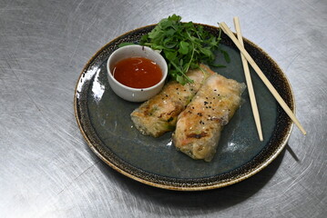 A plate of fresh spring rolls, elegantly arranged and served with a side of sweet chili sauce, placed in front of a blurred background. 