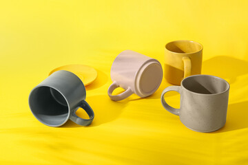 Set of different ceramic mugs and palm leaf shadow on yellow background