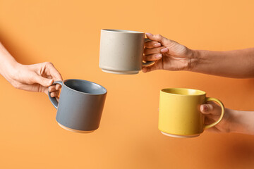 Female hands with ceramic cups on orange background