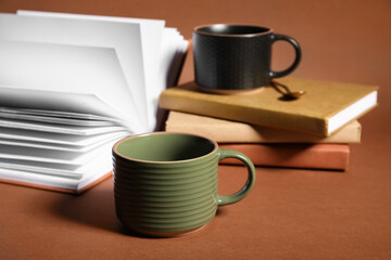 Different ceramic mugs with notebooks on brown background