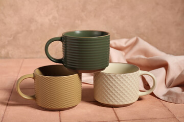 Different ceramic mugs with fabric on beige tile table