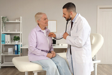 Obraz premium Male doctor with stethoscope listening to mature woman in clinic