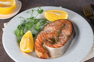 Baked trout steak with lemon, rosemary and garlic on white plate
