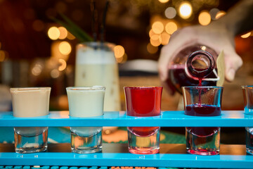 Brightly colored shot glasses filled with a delicious pouring drink that enhances fun