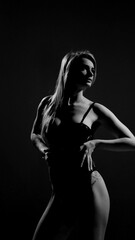 Blonde with a beautiful figure in a black patent leather bodysuit posing in a studio. Studio lighting, low exposure, monochrome image