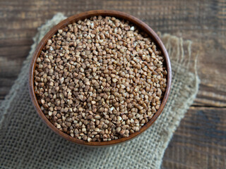 Organic buckwheat groats in a wooden bowl with a spoon on a linen napkin on a wooden table.
