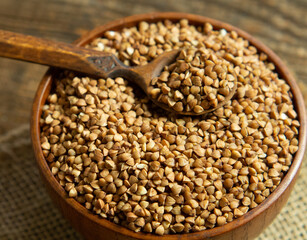 Organic buckwheat groats in a wooden bowl with a spoon on a linen napkin on a wooden table.