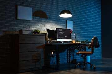 Interior of dark programmer's office with workplace and glowing lamp