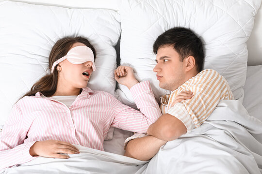 Young annoyed man lying in bed with his snoring wife at home