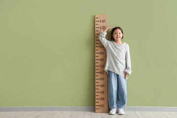 Cute Asian girl measuring height with stadiometer near green wall