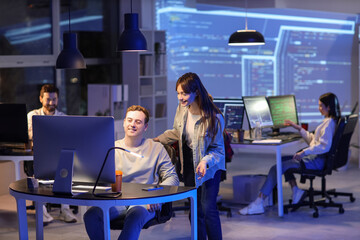 Male programmer working with his colleague in office at night