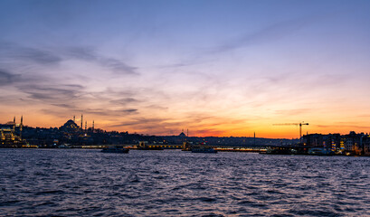 panoramic photograph capturing Istanbul's historic peninsula bathed in a crimson sunset glow. The city's iconic skyline silhouettes against the vibrant evening sky, highlighting its rich architectural