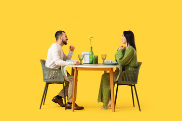 Young couple at restaurant table on yellow background